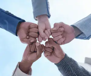 A diverse group of people joining hands in a fist bump, symbolizing the unified connection between a brand and its community. This visual illustrates how an enterprise wallet pass platform rewards the full spectrum of loyalty by incentivizing behavioral actions. It highlights how a digital loyalty card fosters a branded fandom through real-time recognition and rewards for engagement beyond the transaction.