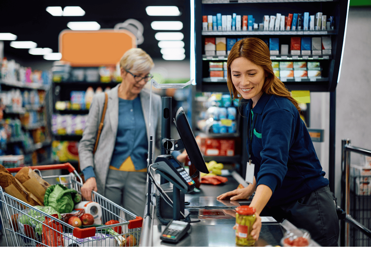 Retail cashier completing a checkout transaction while a customer stands at the till, illustrating low-friction loyalty onboarding in store